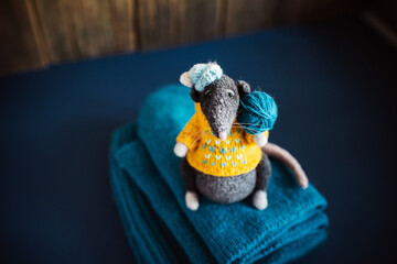 Handmade knitted toy. Amigurumi black rat toy in blue hat and yellow  sweater on the blue and wooden  background . Crochet stuffed animals.