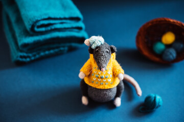 Handmade knitted toy. Amigurumi black rat toy in blue hat and yellow  sweater on the blue and wooden  background . Crochet stuffed animals.