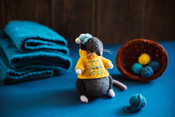Handmade knitted toy. Amigurumi black rat toy in blue hat and yellow  sweater on the blue and wooden  background . Crochet stuffed animals.
