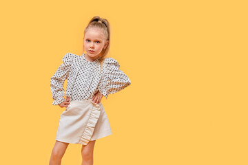A beautiful girl in a polka-dot shirt and short skirt, copy space on the right. Yellow isolated background.