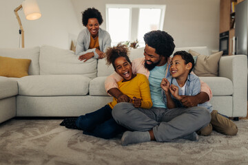Afro family in the living room. Father tickling his children