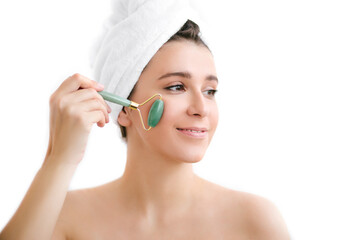 Beautiful young woman with perfect skin wearing towel on head using a jade face roller with natural quartz stones.
