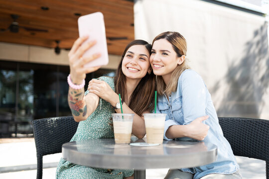 LGBT couple taking a selfie with a smartphone while sitting in a table outside a coffee shop