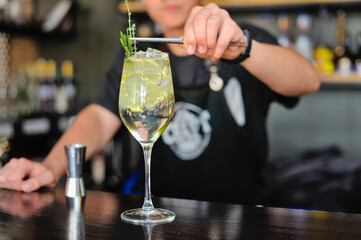 Bartender adds drink and ingredients to cocktail glass on bar counter with bar equipment