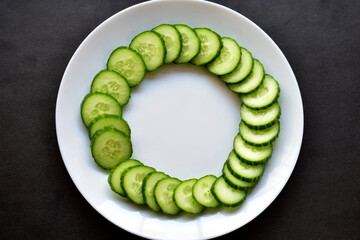 Sliced Green cucumber on a white plate on a black background