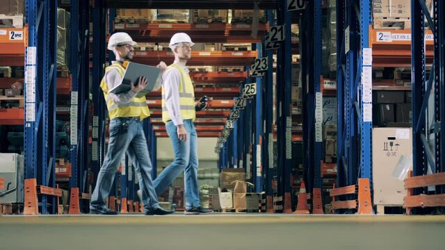 Side view of two warehouse workers moving between racking frames
