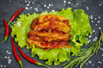 Tasty Bass fish fillets in Mediterranean sauce with tomatoes, olives and capers in baking pan on rustic wooden background with ingredients. Top view