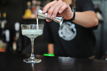 Bartender adds drink and ingredients to cocktail glass on bar counter with bar equipment