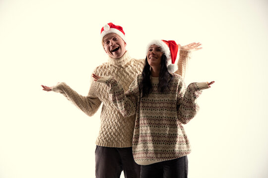 Young couple in Christmas sweaters and hats on white background