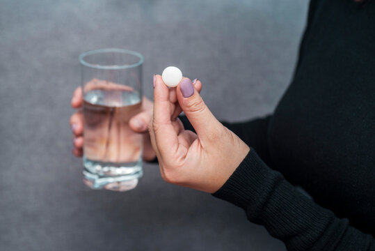 Woman Holds Tablet And Glass Of Water. Female Going To Take Tablet From Headache Or Painkiller Or Abortion Pill Medication Drinking Clear Water From Glass