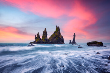 Basalt rock formations Troll toes on black beach with pink sunset clouds. Great purple sky glowing...