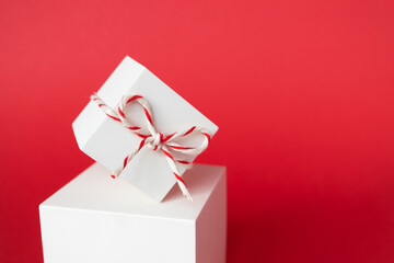 Close-up Christmas gift box with striped twine cotton string balancing on cube podium on red background with copy space