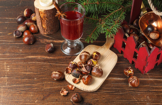 Roasted chestnuts, hot drink in a glass and fir branches on a rough wooden surface, horizontally with space
