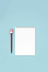 Вlank sheet of paper in notebook and santa claus pen. The concept of making wishes for Christmas. New Year's resolution. Vertical layout, top view, place for text.