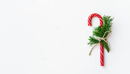 Christmas background with candy canes tied with a rope with fir tree branches on light table. Top view xmas backdrop with space for your greetings. Wide long banner.