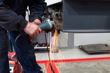 A welder welds and assembles a truck trailer part in a garage. Service of trailers and cars.