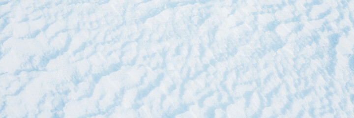 Beautiful winter background with snowy ground. Natural snow texture. Wind sculpted patterns on snow surface. Wide panoramic texture for background and design.