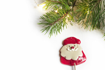 Christmas composition of a natural pine branch with a Christmas composition of a natural pine branch with a garland and a Lollipop in the form of Santa Claus, light background. Corner, frame for banne