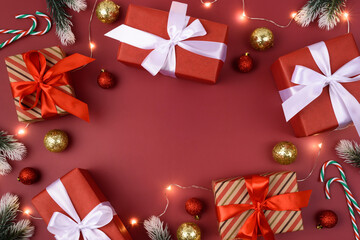 Red background with gifts, decorations, christmas garland and candy cane. Place for text. Xmas flat lay with fir branches. Copyspace in the middle. Nobody.