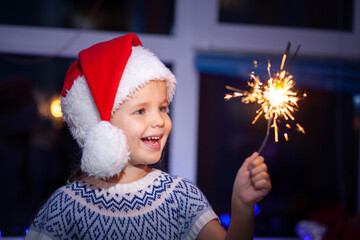 Festive Merry Christmas sparklers. Portrait of a cute little girl holding sparklers, new year 2021,...