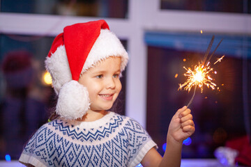 Festive Merry Christmas sparklers. Portrait of a cute little girl holding sparklers, new year 2021,...