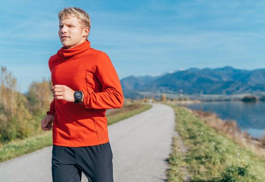 A man dressed in red long sleeve shirt have a morning jogging by the road with a mountain background. Sporty people activities and a healthy lifestyle concept image.