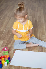 child girl draws a large picture with gouache paints sitting on the floor.