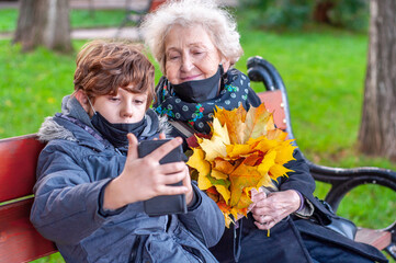 Happy elderly woman and teenager boy in a black protective masks with bouquet of fallen leaves in...