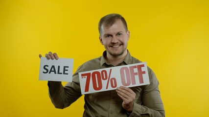 Great discounts. Happy joyful blonde man showing Sale word and showing Up To 70 percent Off purchase inscription. Shopping with low prices, Black Friday concept. Yellow background