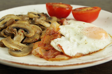 Breakfast recipe. Fried egg with bacon, fried mushrooms,  and tomatoes on a white plate. 