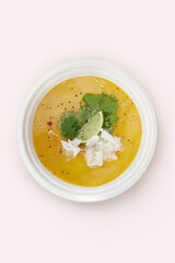 Sopa de batata en bowl descartable biodegradable sobre fondo rosa con topping de lima, coco rallado, perejil y pimiento