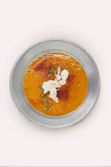 Sopa de calabaza en plato de metal con leche de coco topping de pimentón, coco rallado y semillas de calabaza