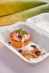 Postre para llevar de pomelo rosado asado granola yogurt coco rallado y menta en descartable biodegradable blanco ambiente tropical fondo rosa hoja de bananero