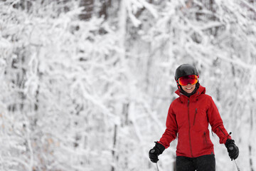 Fototapeta na wymiar Winter sport happy skier Alpine skiing going dowhill against snow covered trees background during winter snowstorm. Woman in red jacket and goggles.