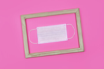 Medical protective face mask in a wooden frame on pink background. Top view. Flat lay. Concept of protecting a person from virus or allergy. Poster