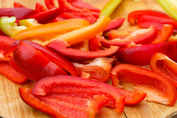 Slices red and yellow sweet peppers on wooden cutting board