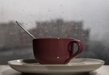 A cup of hot tea in the background rain outside the window. Selective focus.