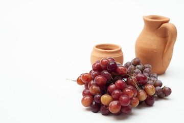 Champagne grape and Red Globe grape in front of jar and clay glass on a white background, with space for art.