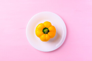 Yellow bell pepper on white plate with pink background, Top view