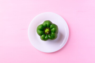 Green bell pepper on white plate with pink background, Top view