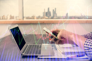 Double exposure of man's hands holding and using a digital device and forex graph drawing. Financial market concept.