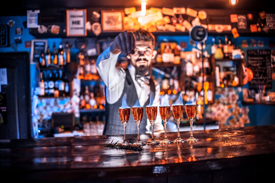 Confident barman pouring fresh alcoholic drink into the glasses on the bar