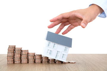 One hand grabs the small house model and there is a row of declining dollar coins