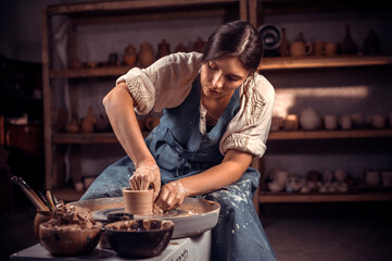 Charming craftsman works with clay on a potter's wheel. The concept of craft creativity. - obrazy, fototapety, plakaty