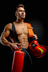 portrait of a muscular, handsome firefighter on a dark background, holding a fire helmet, looking...