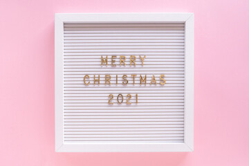 Letter board with Merry Christmas 2021 greeting, greeting quote on letterboard on pink pastel girly backdrop. Flat lay, from above, minimal style