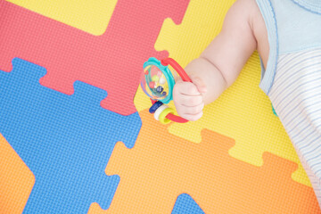 Baby hand holding a rattle on a colored rubber mat puzzle for playing foam with geometric figures