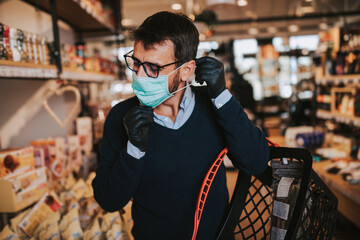 Casually dressed middle age man with face protective mask and gloves buying healthy food and drink...