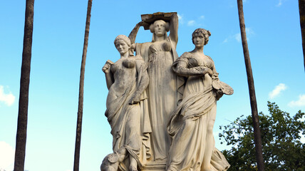 3 statues of women representing the arts as muses with palm trees in the background 