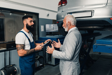 Car mechanic talking with senior business man costumer during periodic car condition check. Technical inspection station.